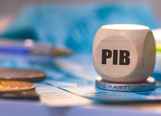 Imagem de um dado com a inscrição "PIB" sobre uma moeda de real - Metrópoles
